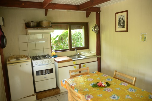 Cuisine d'un bungalow avec une cuisinière, un évier et une table à manger, décorée d'une nappe jaune et d'une fleur.