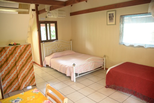 Intérieur d'un bungalow avec un lit double, un lit simple, une kitchenette et un espace de vie lumineux.