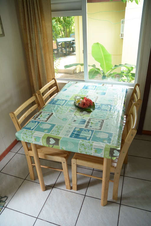 Table en bois avec des chaises, recouverte d'une nappe colorée, placée près d'une fenêtre donnant sur un jardin.