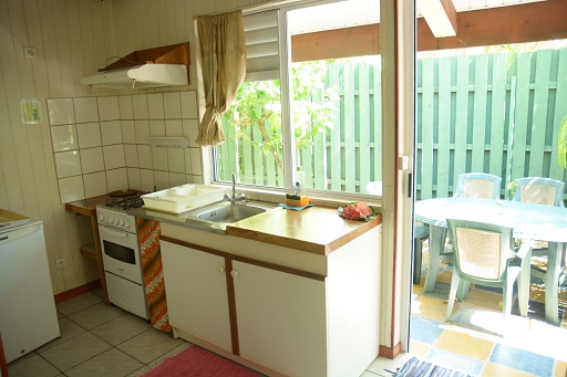 Vue intérieure d'un bungalow avec une cuisine équipée, incluant un évier, cuisinière et accès à une terrasse extérieure avec table et chaises.